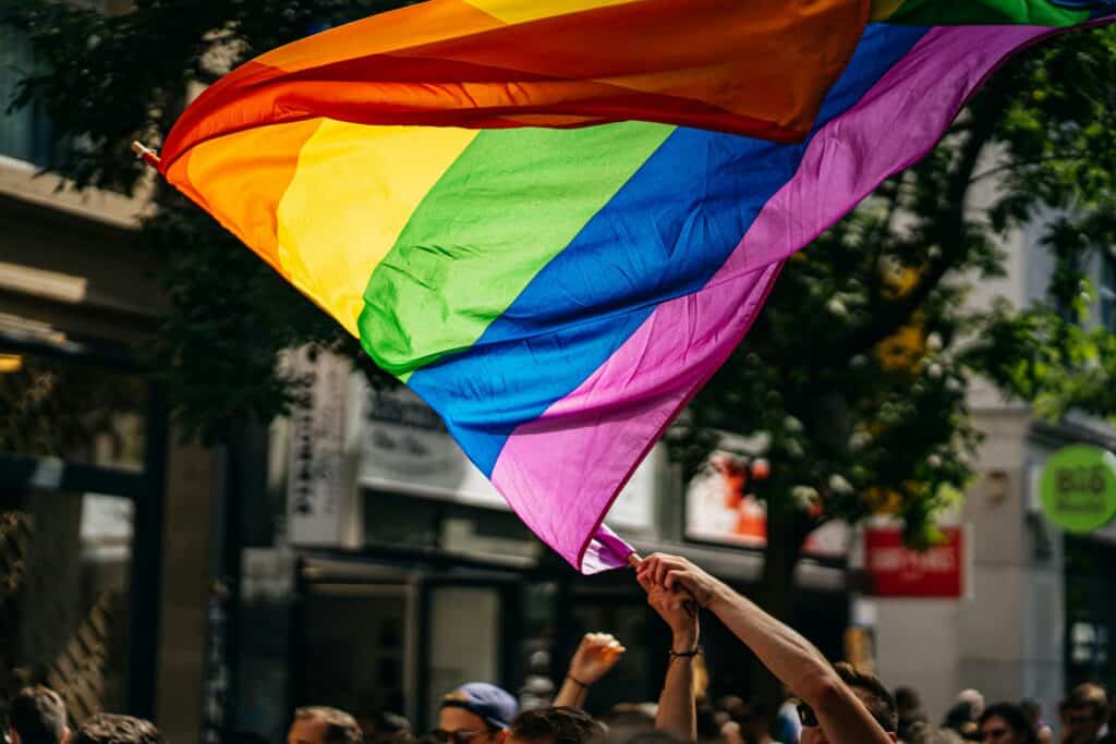 A large rainbow flag is being held up by a person in a group of people.