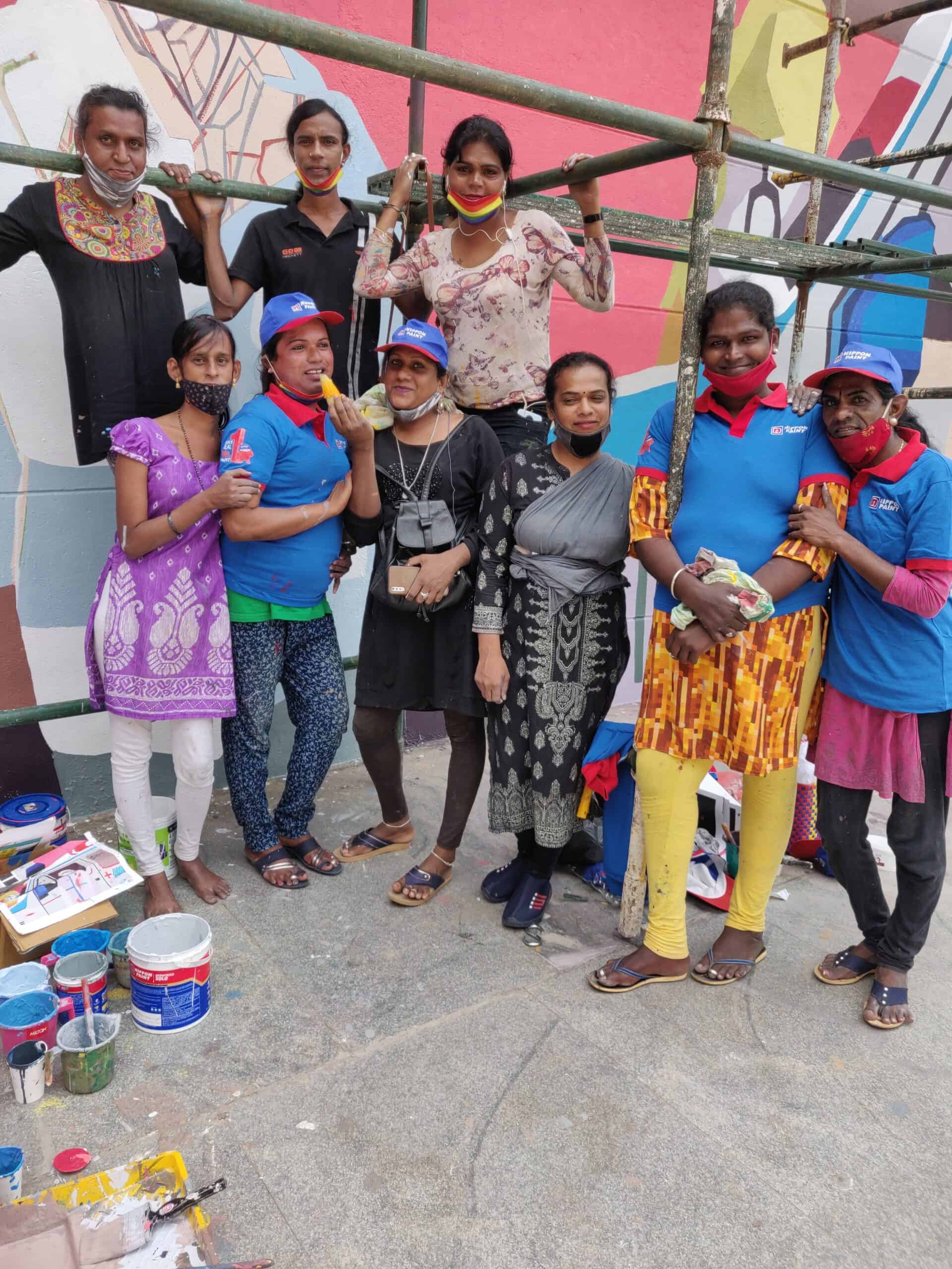 Aravani members and local helpers stand in front of a mural for a group photo.