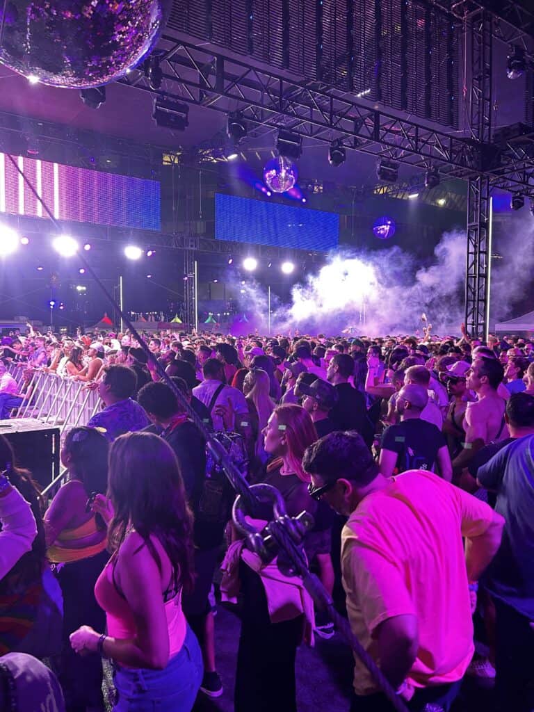 A crowd of people surrounding a stage bathed in purple light at the OUTLOUD concert. Credit: Blossom Brown