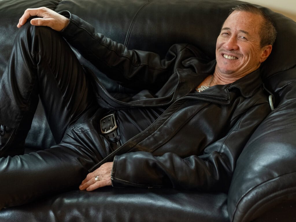 Willy Wilkinson smiling at the camera sitting on a dark leather couch.