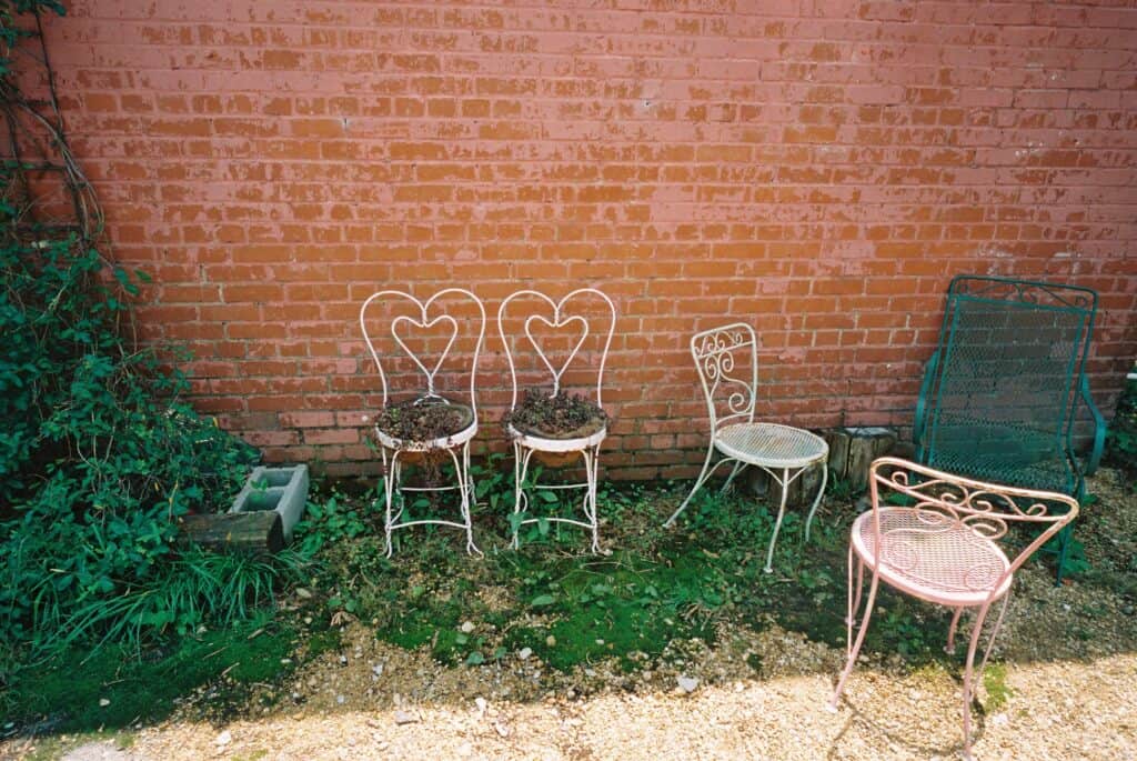 Two chairs with hearts and a few other metal wire chairs in front of a brick wall.