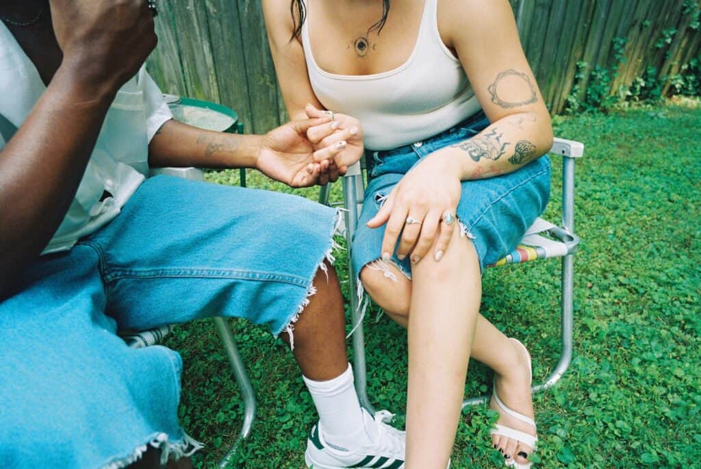 Close up of Miss B Haven and Wilson holding hands as they sit on chairs in the yard.