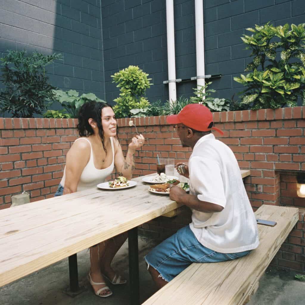 Miss B Haven and Wilson sitting across from each other at a table eating food.